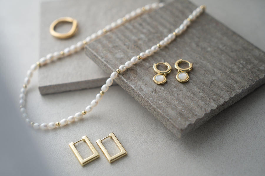 Gold jewelry including earrings and necklaces on a stone surface