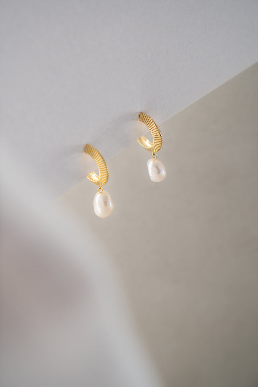 Gold earrings with pearl drops on a neutral background