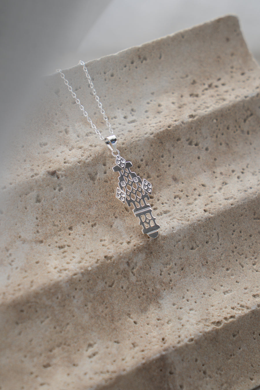Silver necklace with a decorative pendant on a textured stone surface