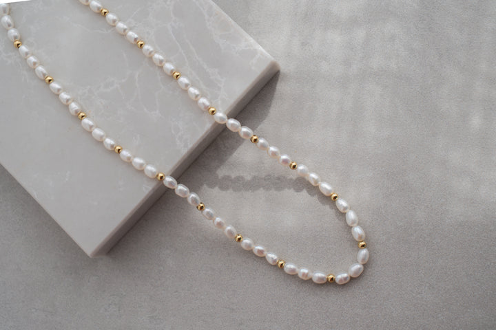 Pearl necklace with gold beads on a light gray surface