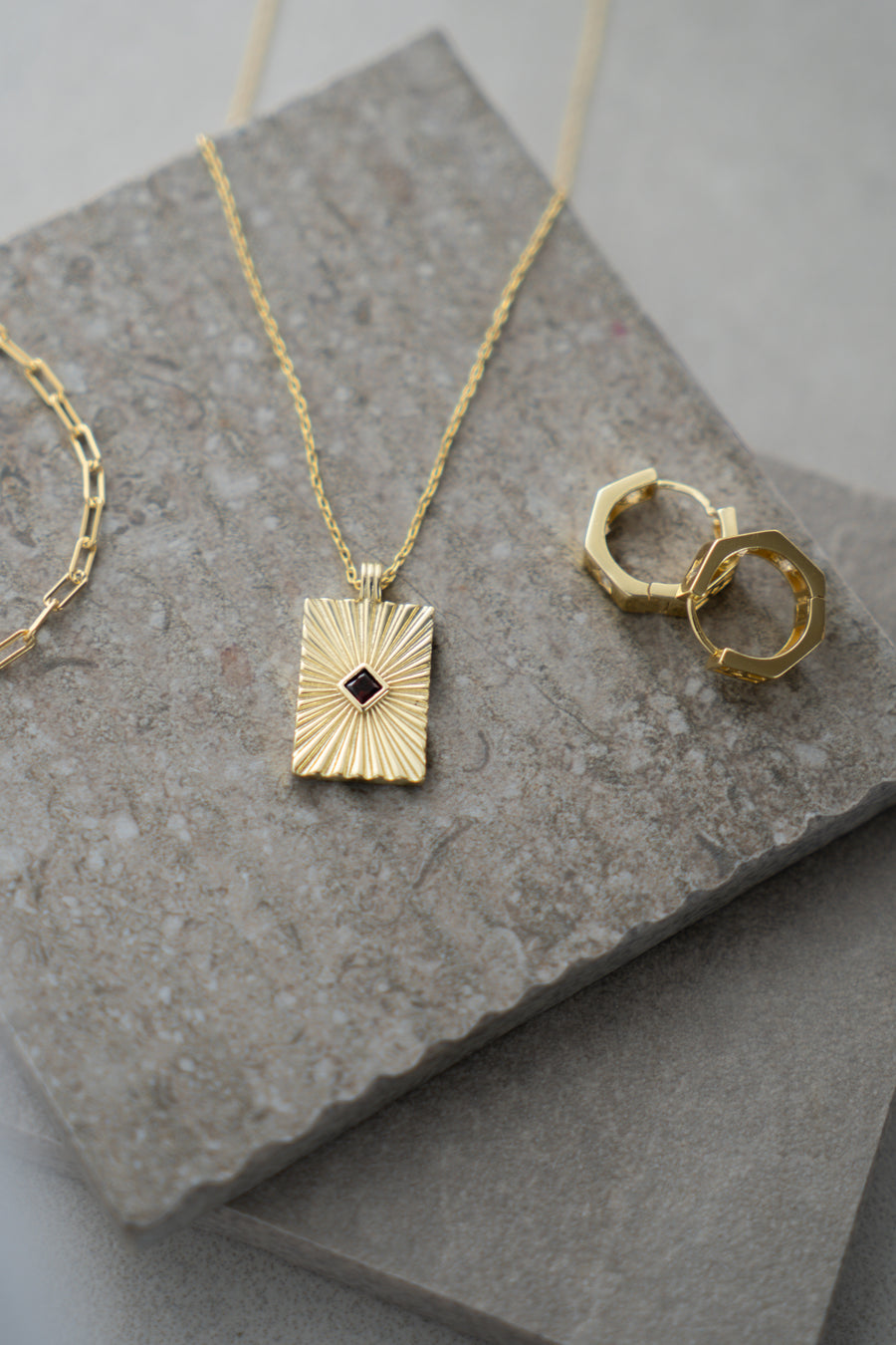 Gold necklace and earrings on a stone surface