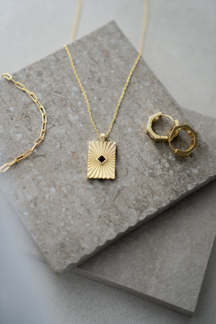 Gold necklace and earring on a textured stone surface