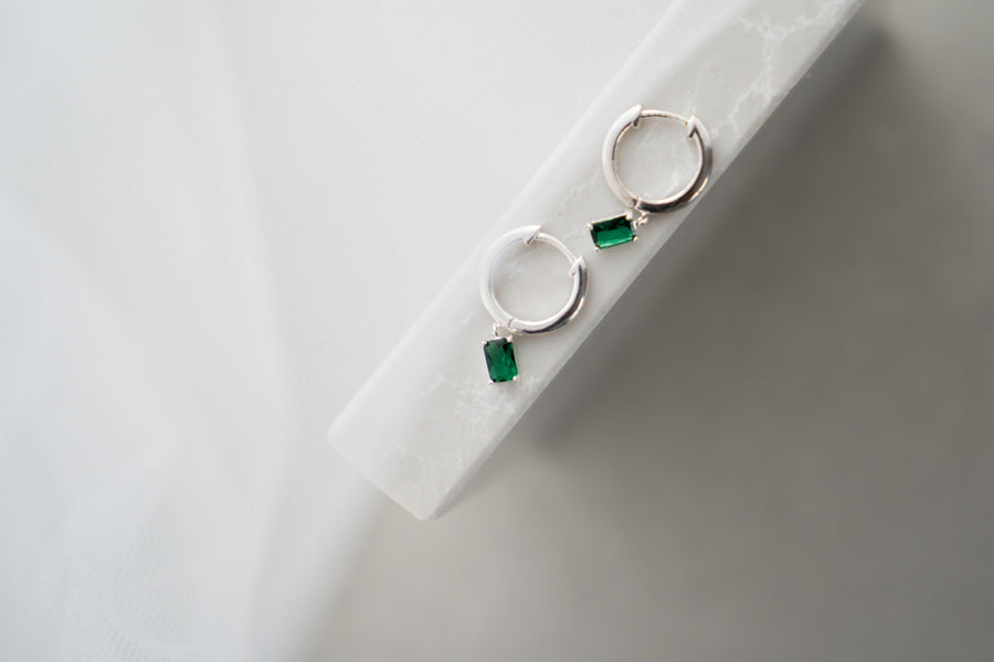 Silver earrings with green gemstones on a white surface