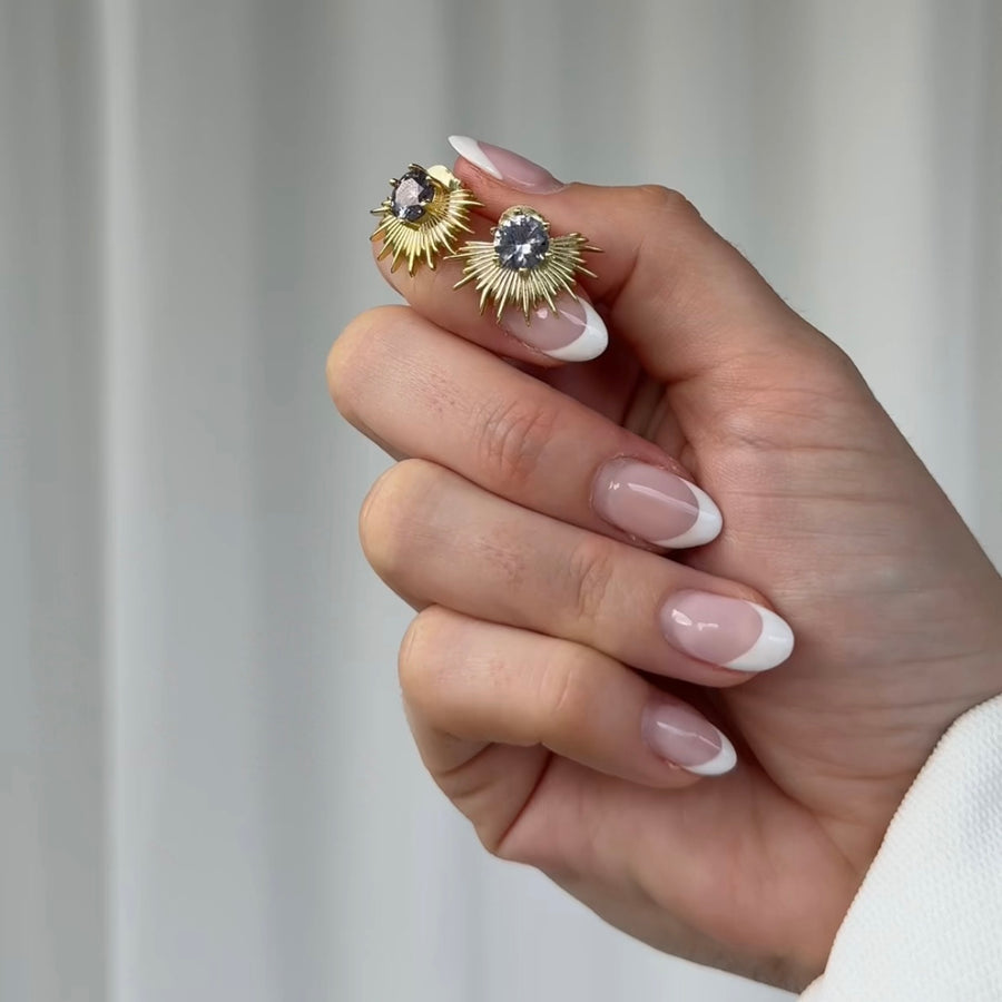 Hand holding a pair of gold earrings with a neutral background