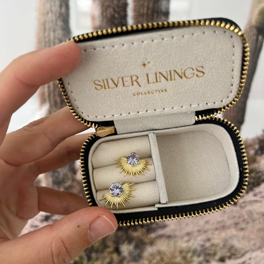 Gold earrings in a 'Silver Linings' jewelry case held by a hand.